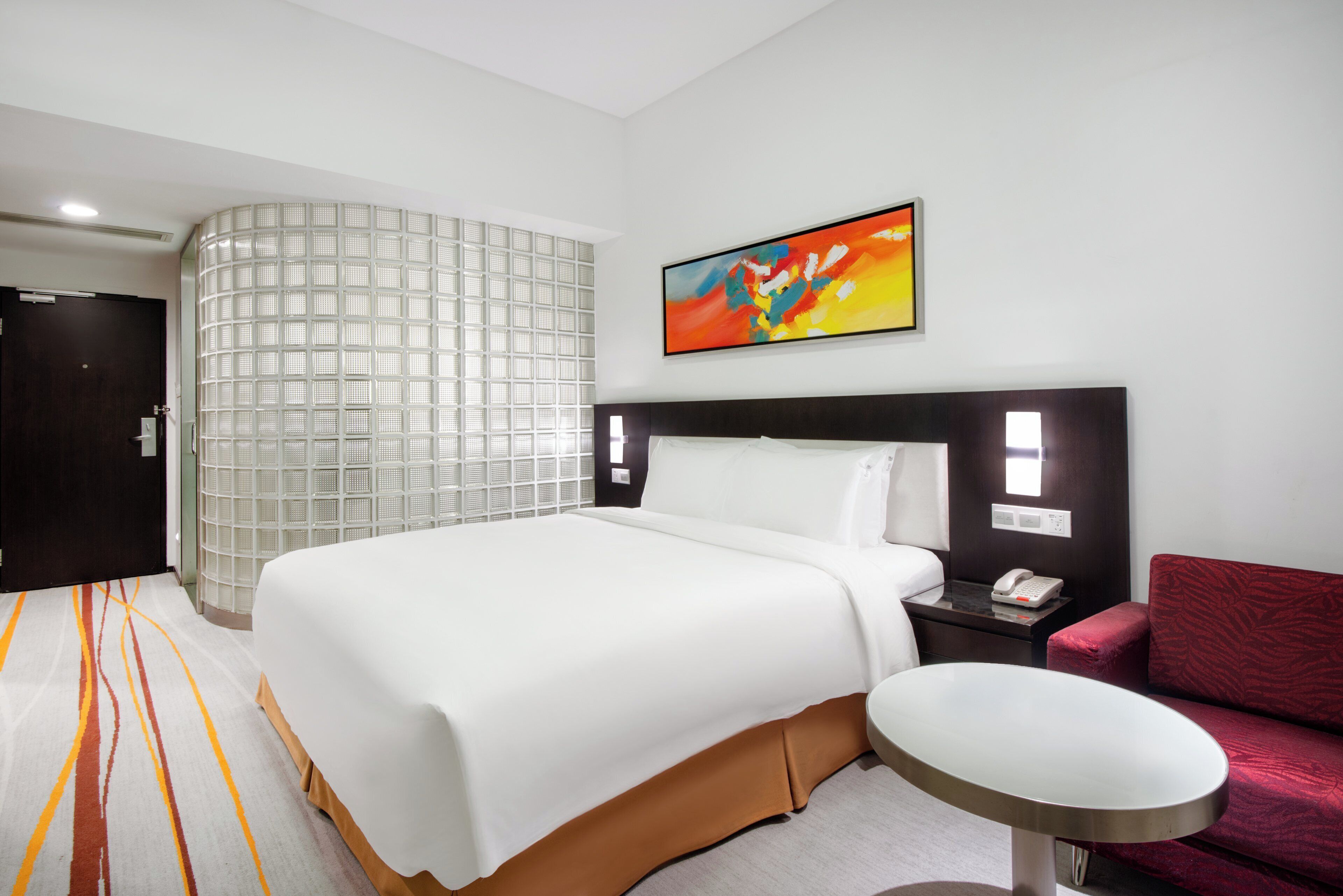 Habitación de hotel con cama, escritorio, silla, un cuadro y un panel decorativo en la pared.