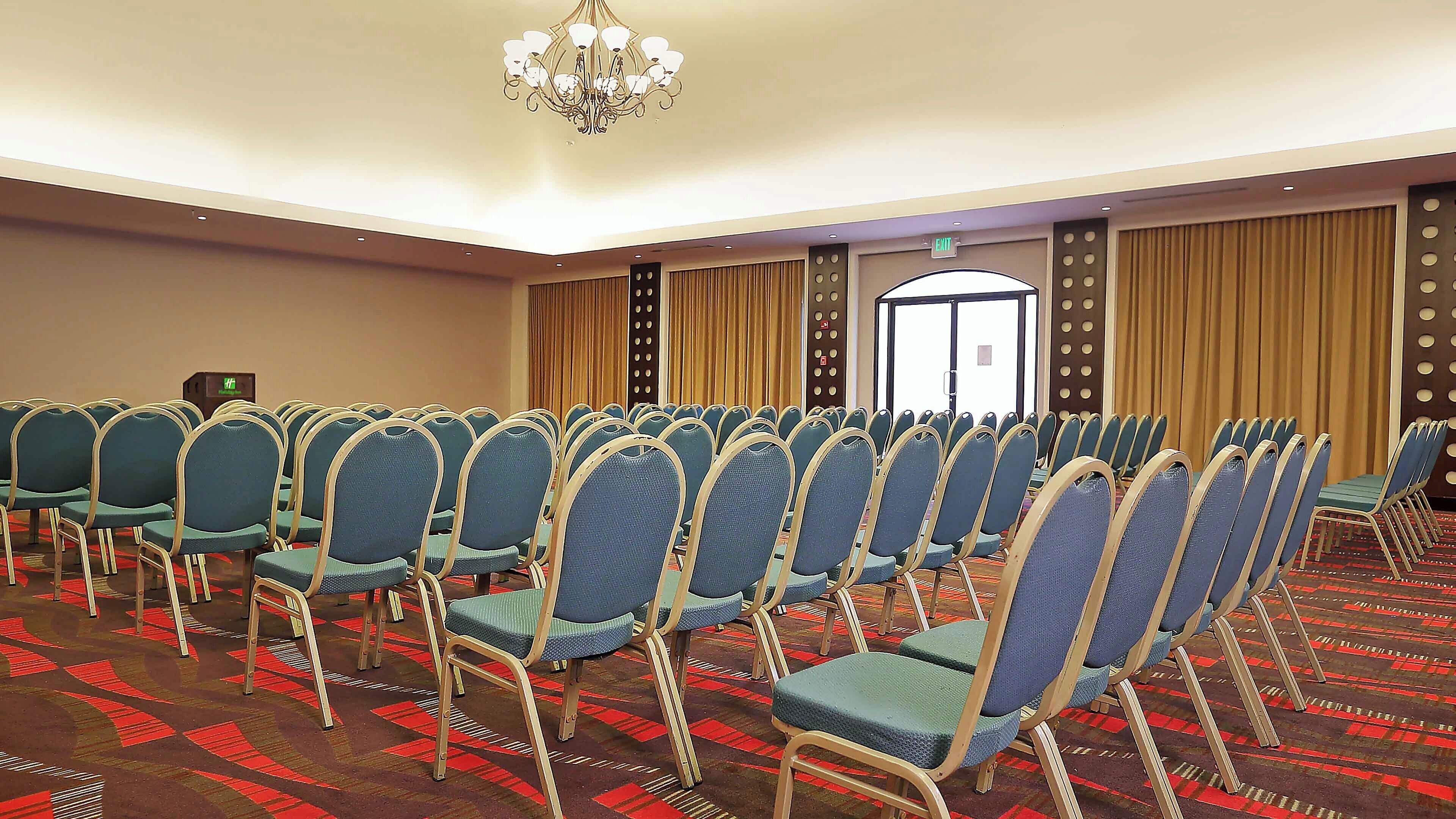 A conference room with rows of chairs, a chandelier, and a patterned carpet.