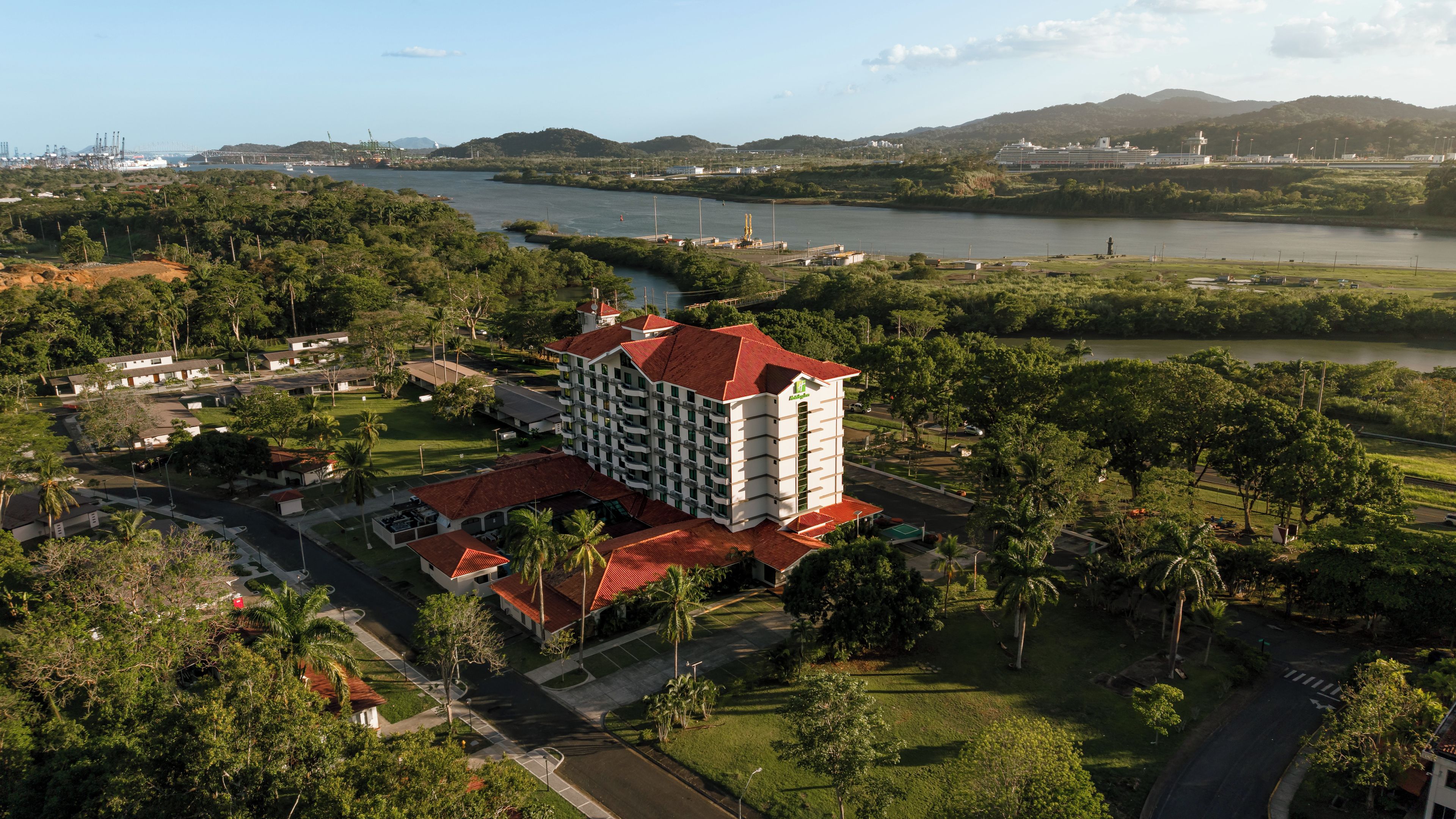 A hotel with multiple floors, surrounded by lush greenery and a body of water.