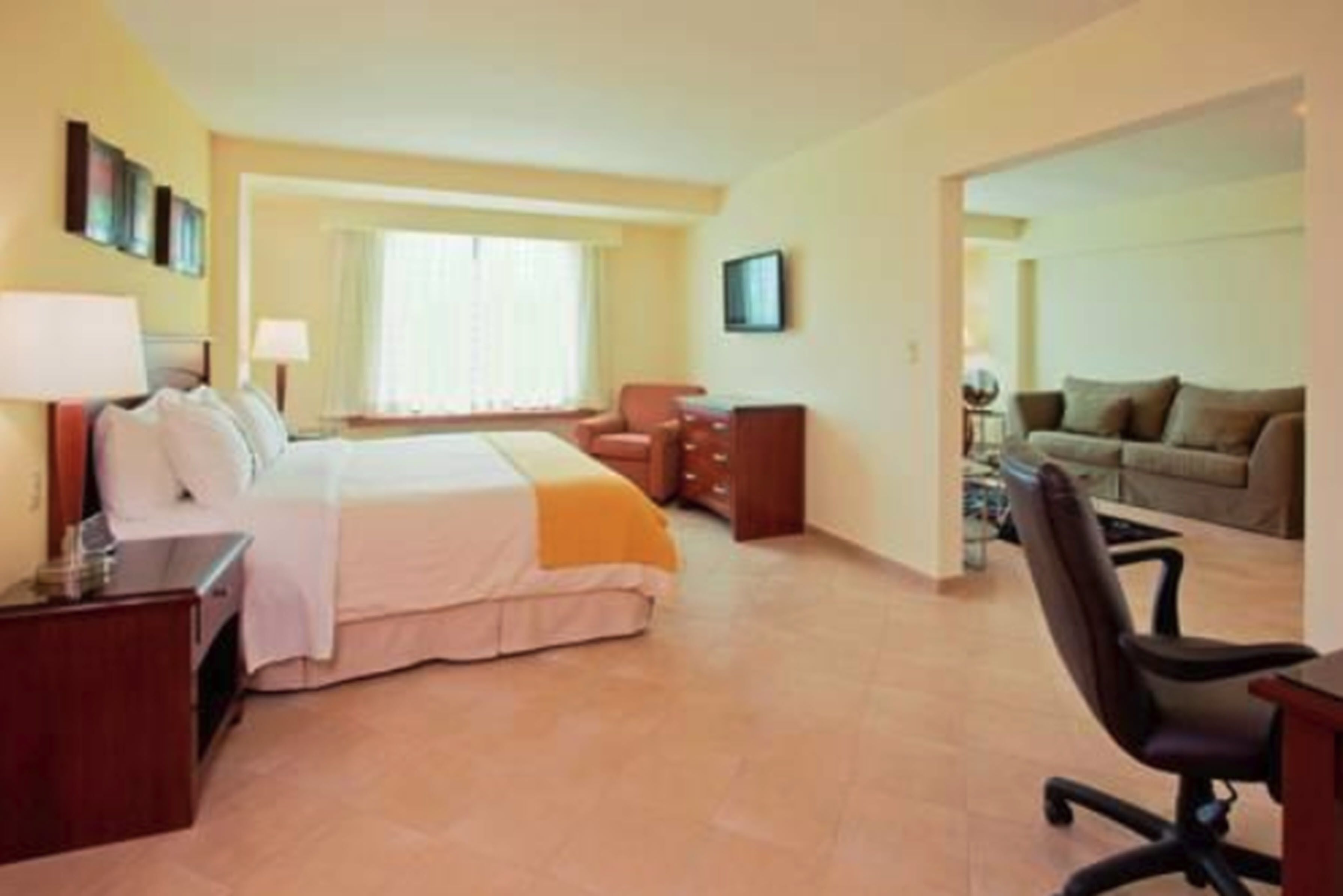 A hotel room with a bed, a desk, a chair, a sofa, and a TV.