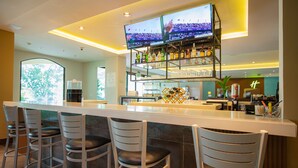 A bar area with a long counter, multiple bar stools, and a television screen displaying a sports event. - Holiday Inn Panama Canal by IHG (Panama City)