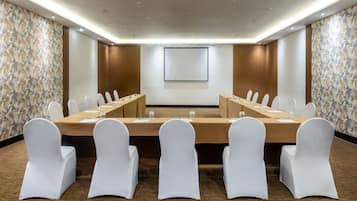 A conference room with a long table, white chairs, and a projector screen.