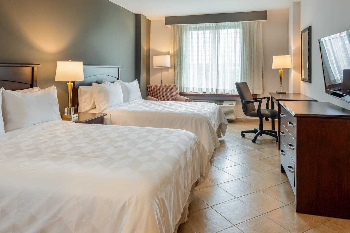 A hotel room with two beds, a desk, a chair, a TV, and a window with curtains.