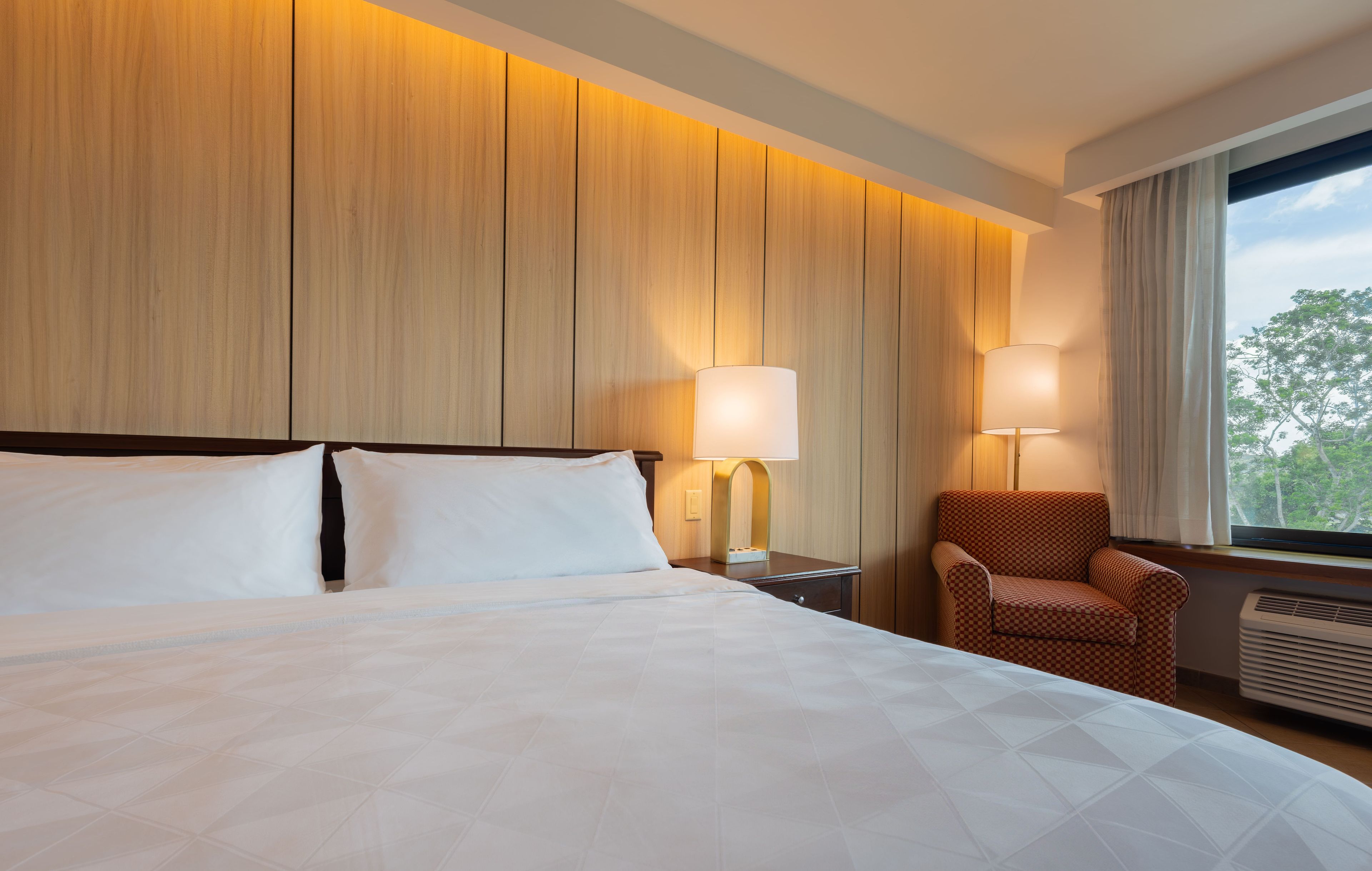 Una habitación de hotel con una cama grande, dos lámparas de noche, una silla y una ventana con vistas.