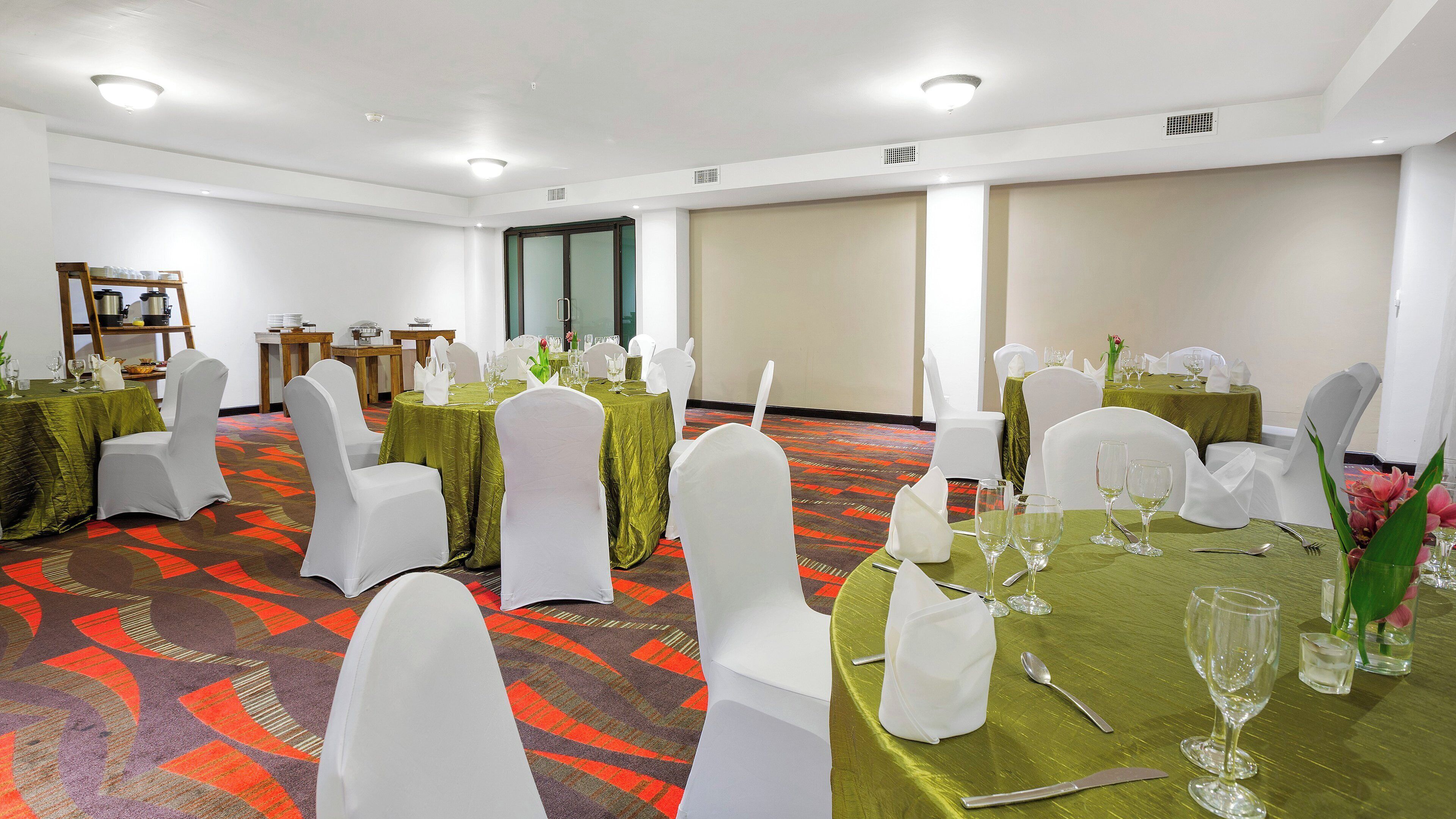 A banquet hall with round tables, white chairs, and green tablecloths.