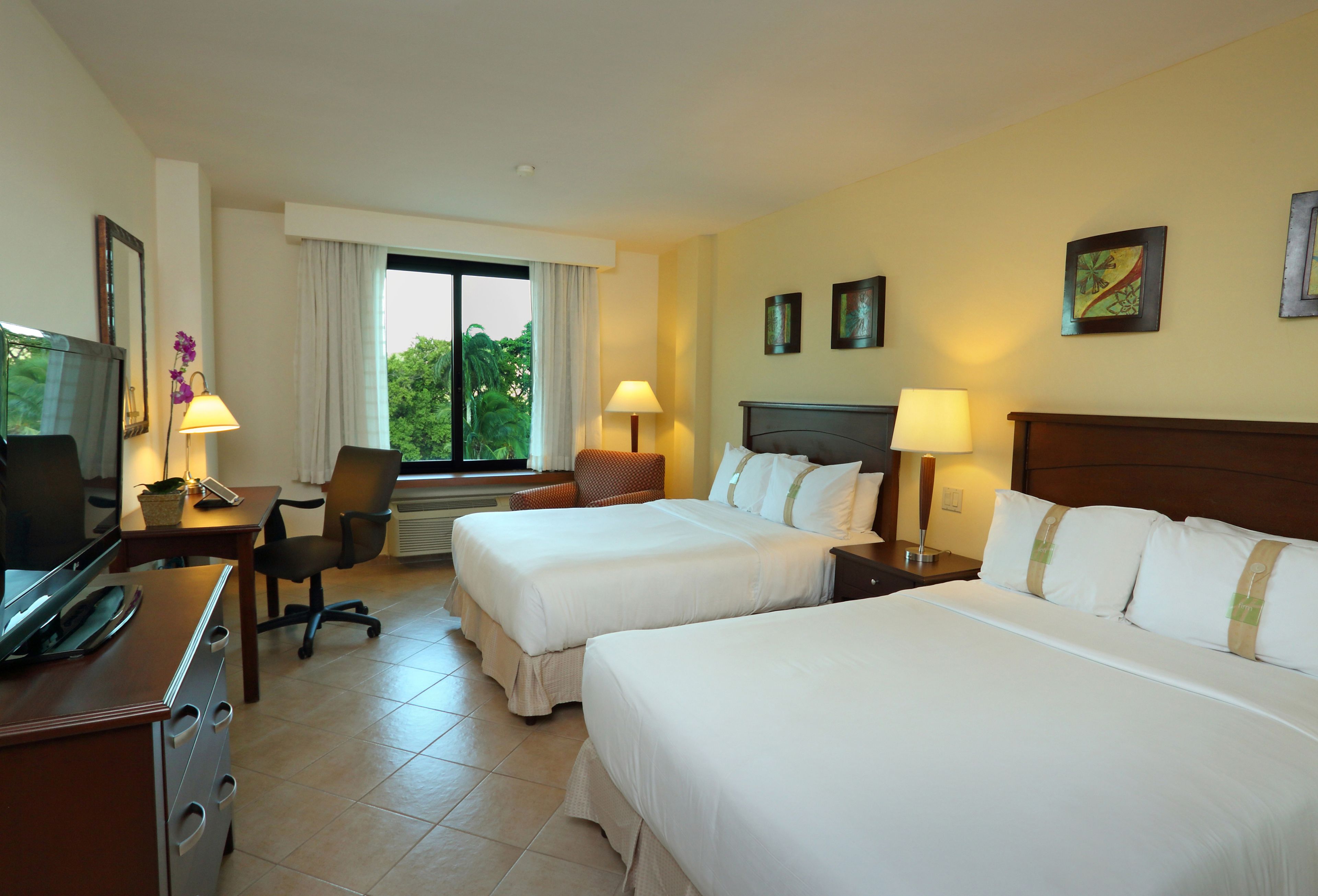 A hotel room with two beds, a desk with a computer, a chair, and a TV.