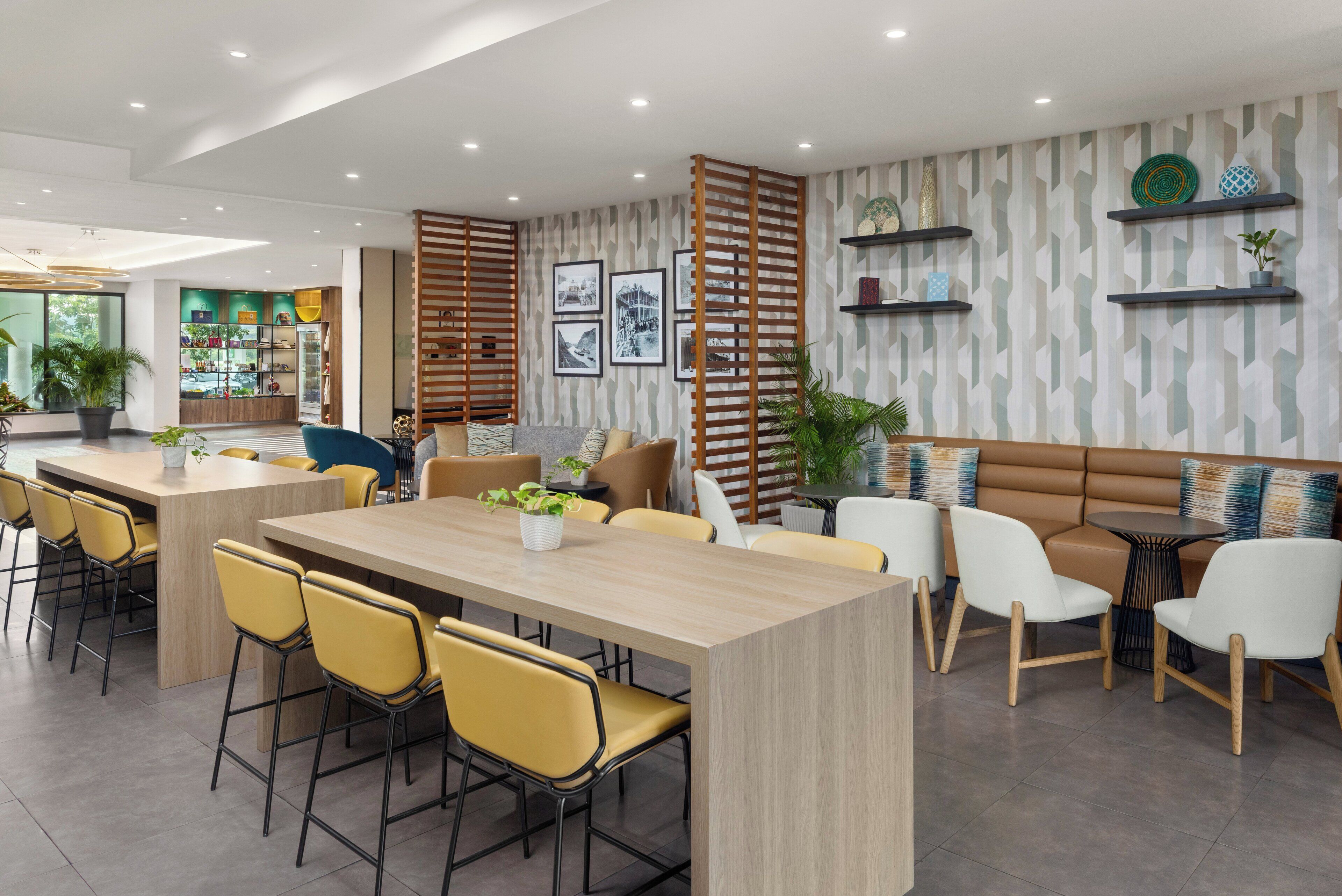 Un comedor moderno con una mesa de madera larga, sillas amarillas y una zona de estar con un sofá marrón y sillas blancas.