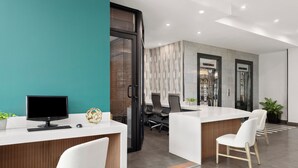 A modern reception area with a teal accent wall, a reception desk, two white chairs, and a computer monitor. - Holiday Inn Panama Canal by IHG (Panama City)