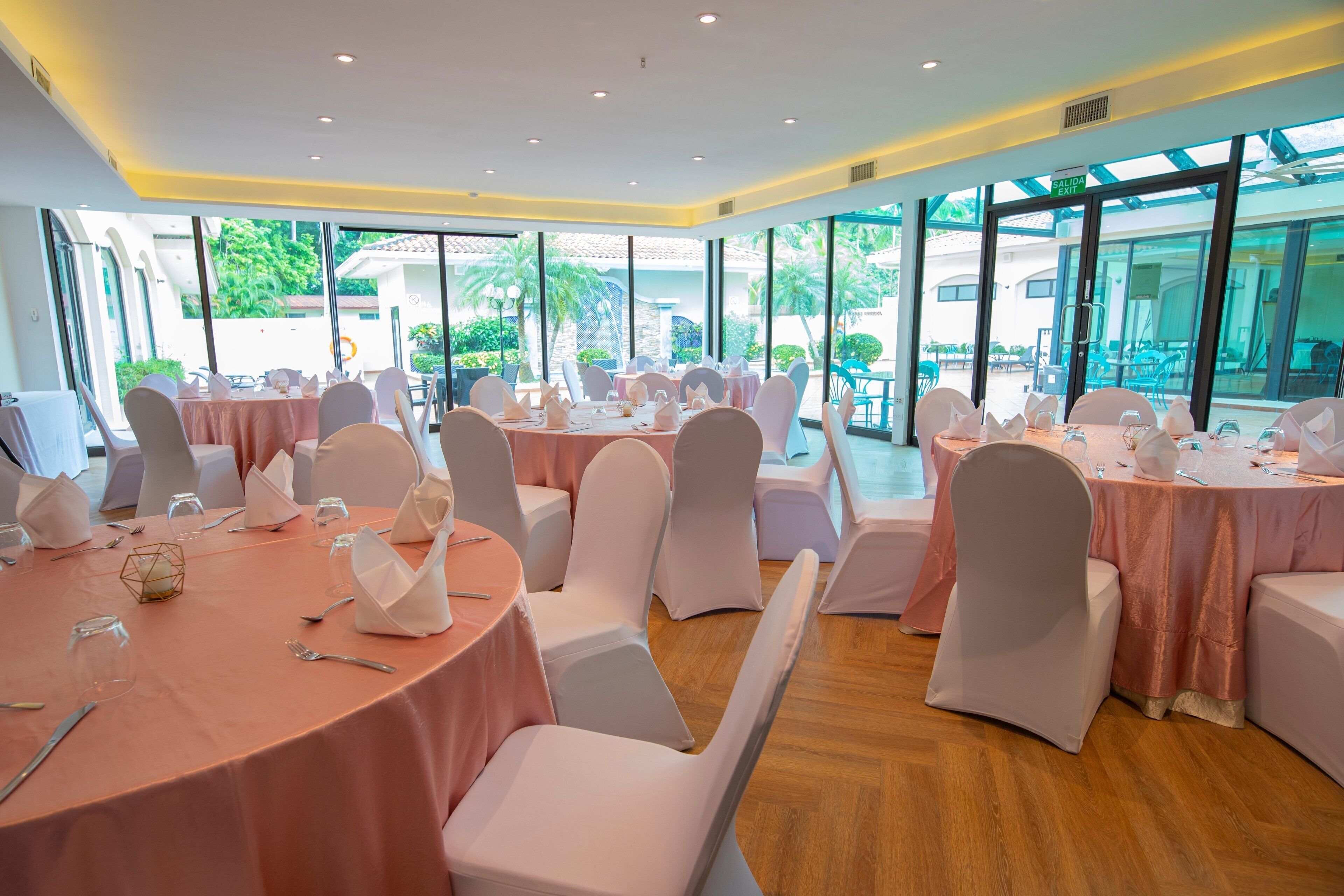 Un salón de banquetes con mesas redondas, sillas blancas y vistas al exterior.