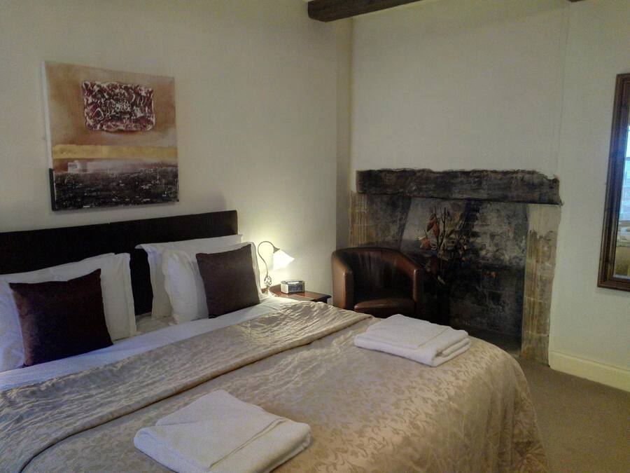 Ein Hotelzimmer mit einem großen Bett, einem Kopfteil, einem Nachttisch mit Lampe, einem Sessel, einem Kamin und einem Wandbild.
