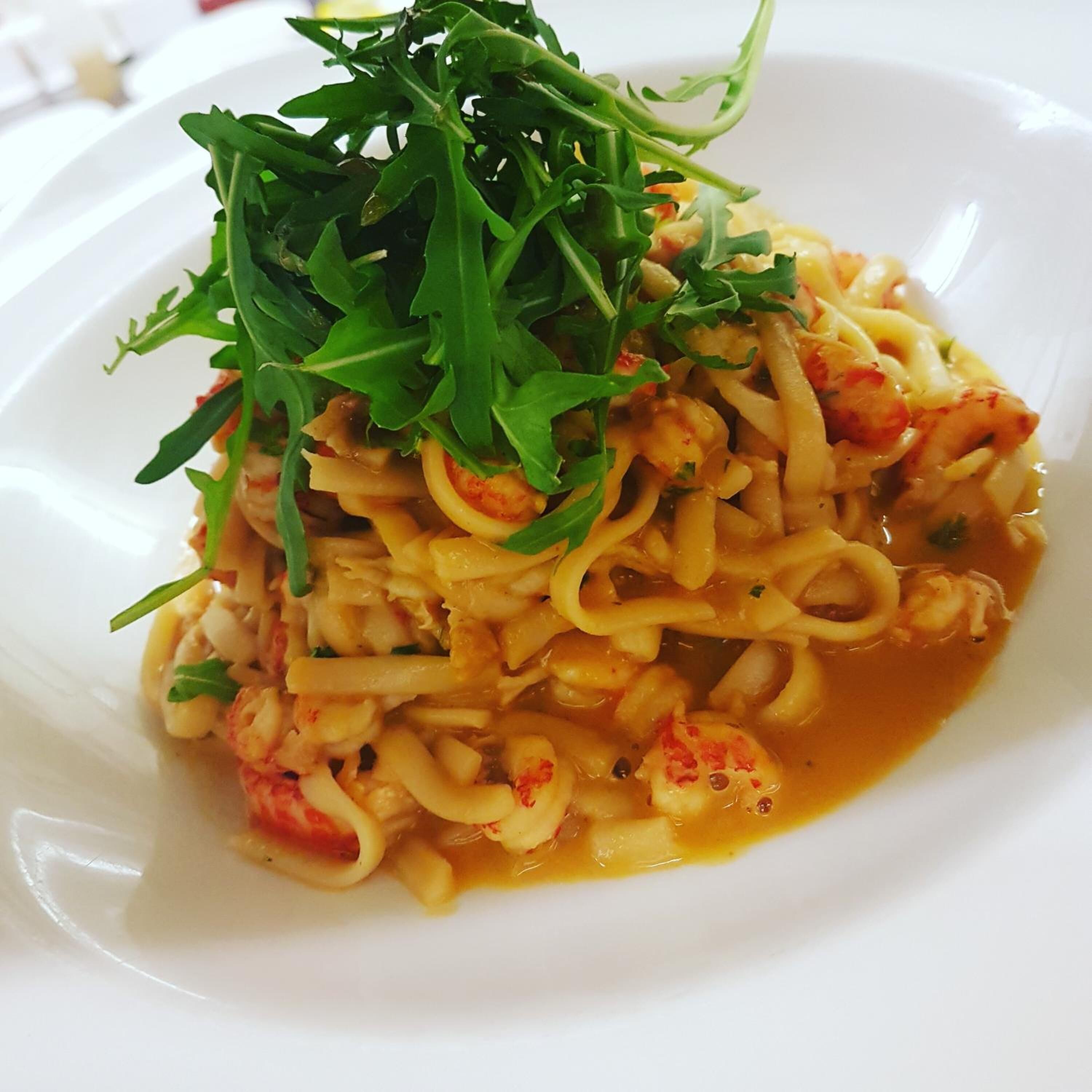 A plate of pasta with shrimp and a garnish of green leaves.