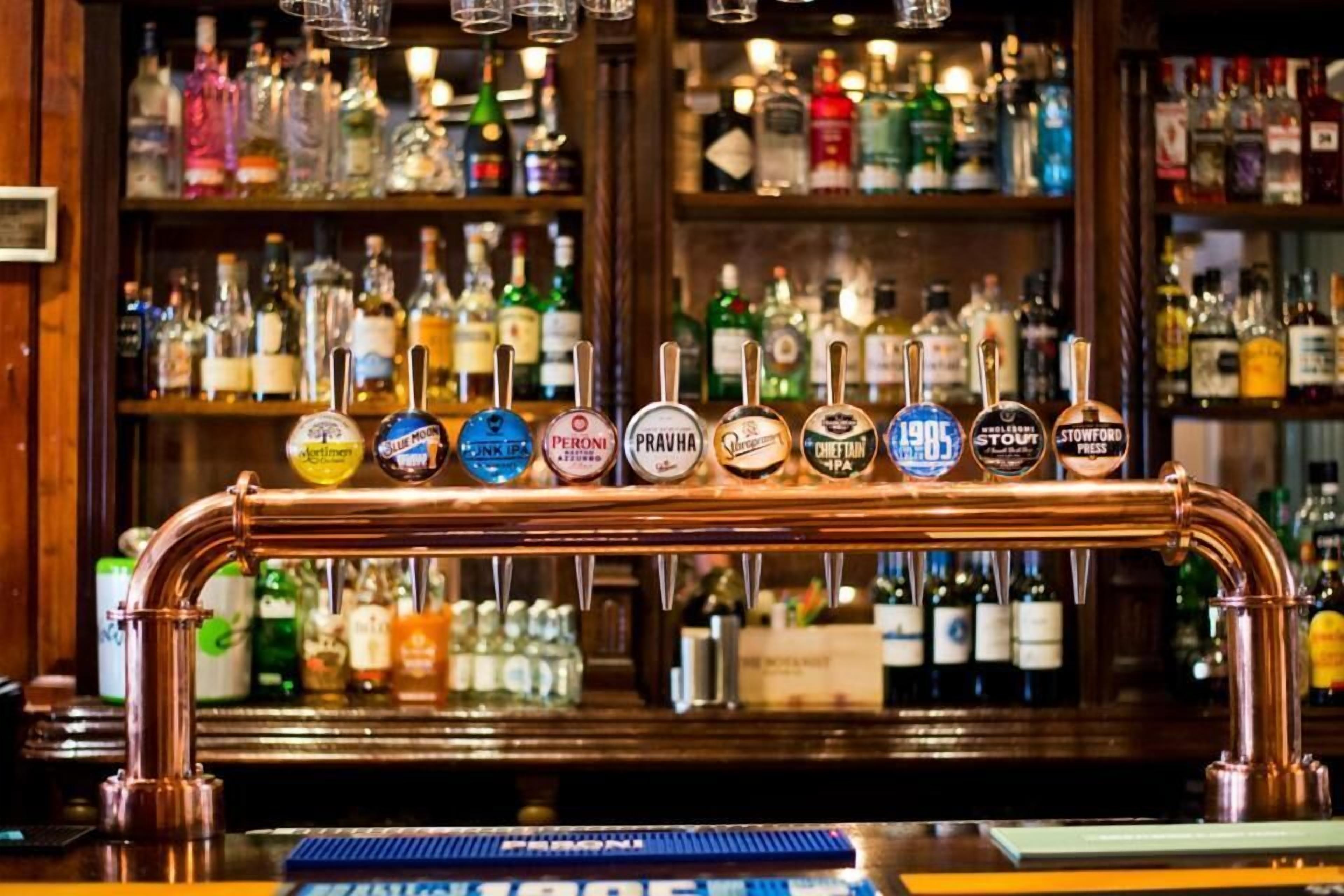 Een bar met een koperen biertap en verschillende andere bierkraaninstallaties, waaronder merken zoals Peroni en Stowford.