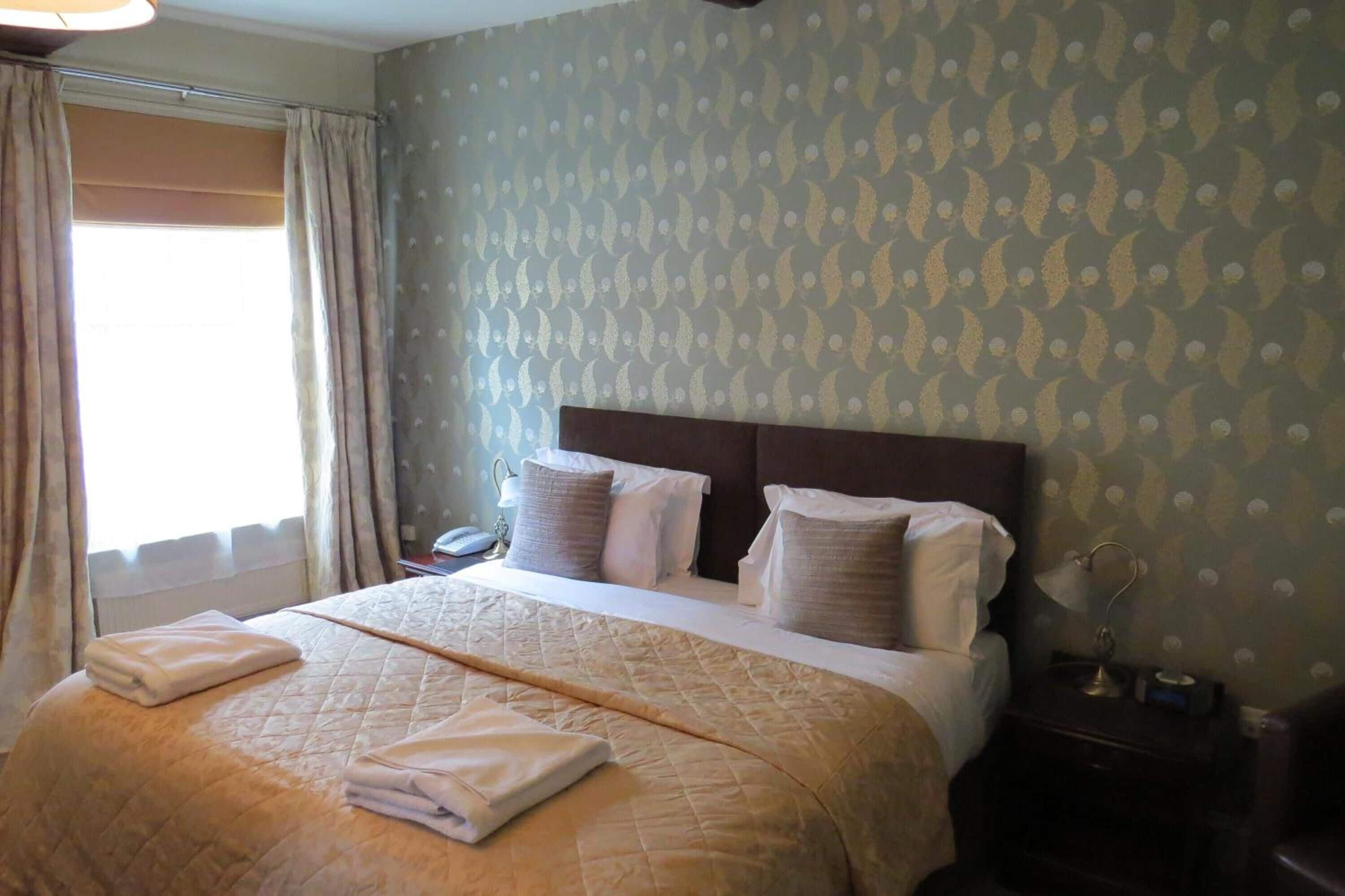 A hotel room with a bed, a nightstand, a lamp, and a window with curtains.