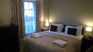 A hotel room with a bed, bedside lamps, a window with curtains, a dresser, and a bottle on the dresser.