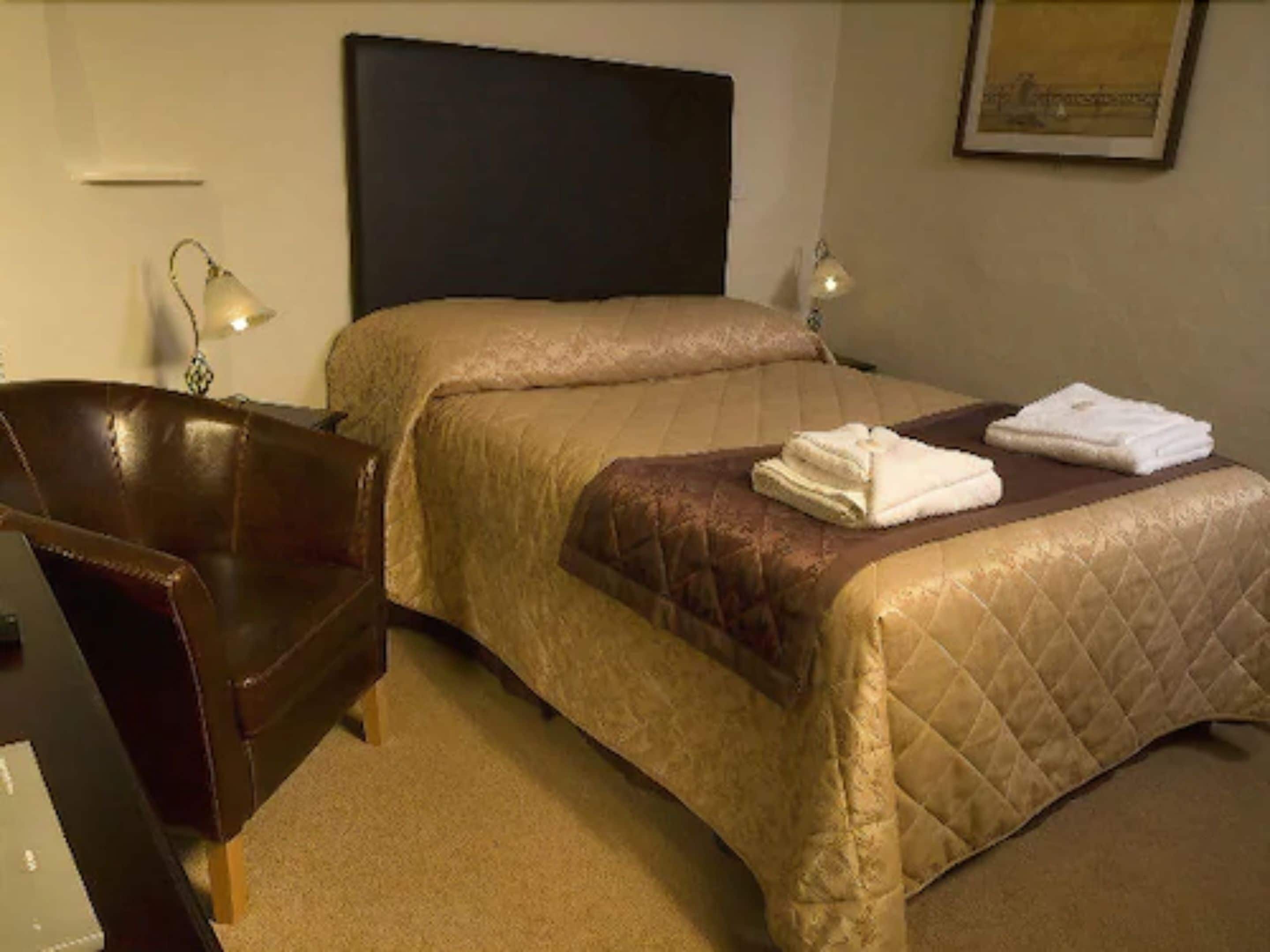 Una habitació d'hotel amb un llit, una cadira, escriptori i una làmpada.