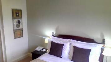 A neatly made bed with white linens and two dark pillows, a bedside table with a lamp, and a wall-mounted air conditioning unit.