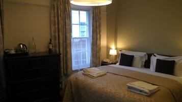 A hotel room with a bed, a dresser, a nightstand, a lamp, and a window with curtains.