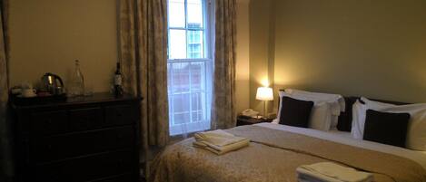 Una habitación de hotel con cama, cómoda, mesita de noche, lámpara y ventana con cortinas.