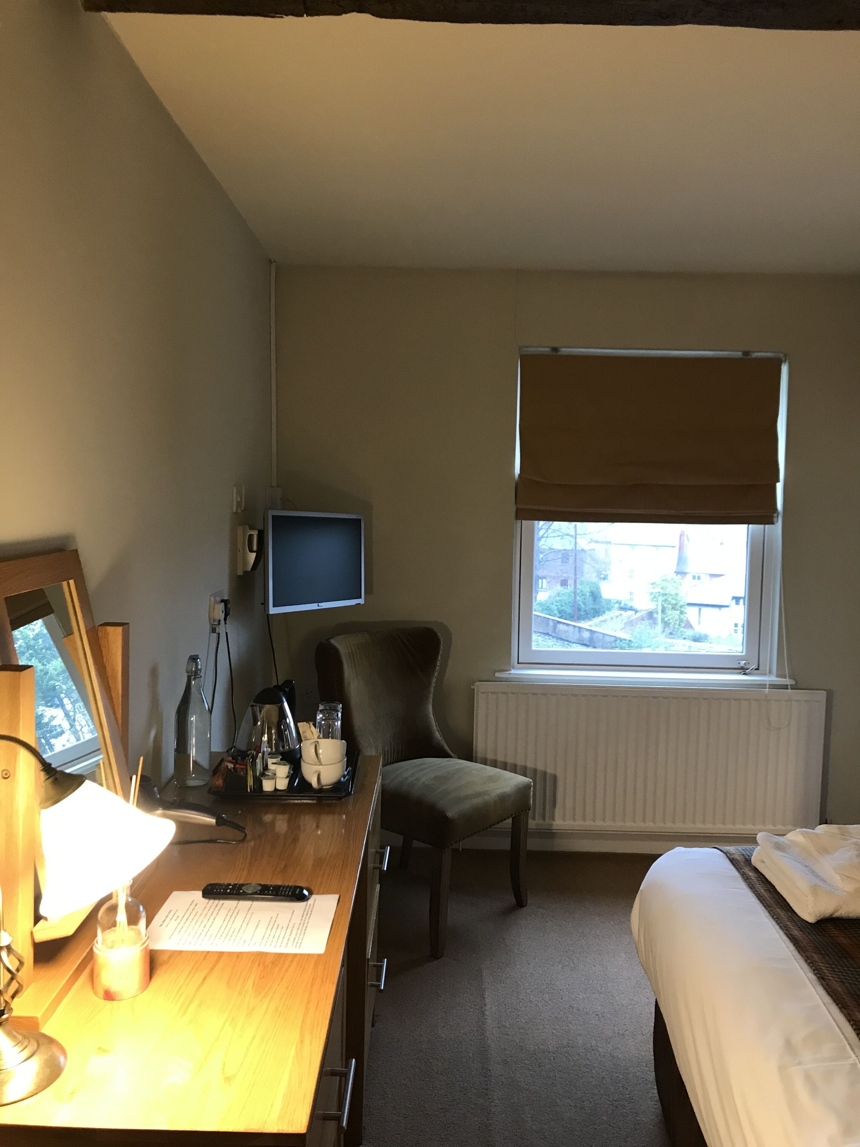 A hotel room with a wooden desk, a chair, a bed, a TV, and a window with a view of buildings.