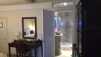 A hotel room with a desk, chair, mirror, and a bathroom with a shower and sink.