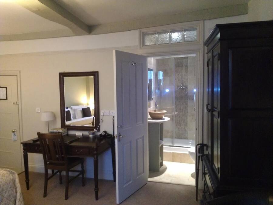 A hotel room with a desk, chair, mirror, and a bathroom with a shower and sink.