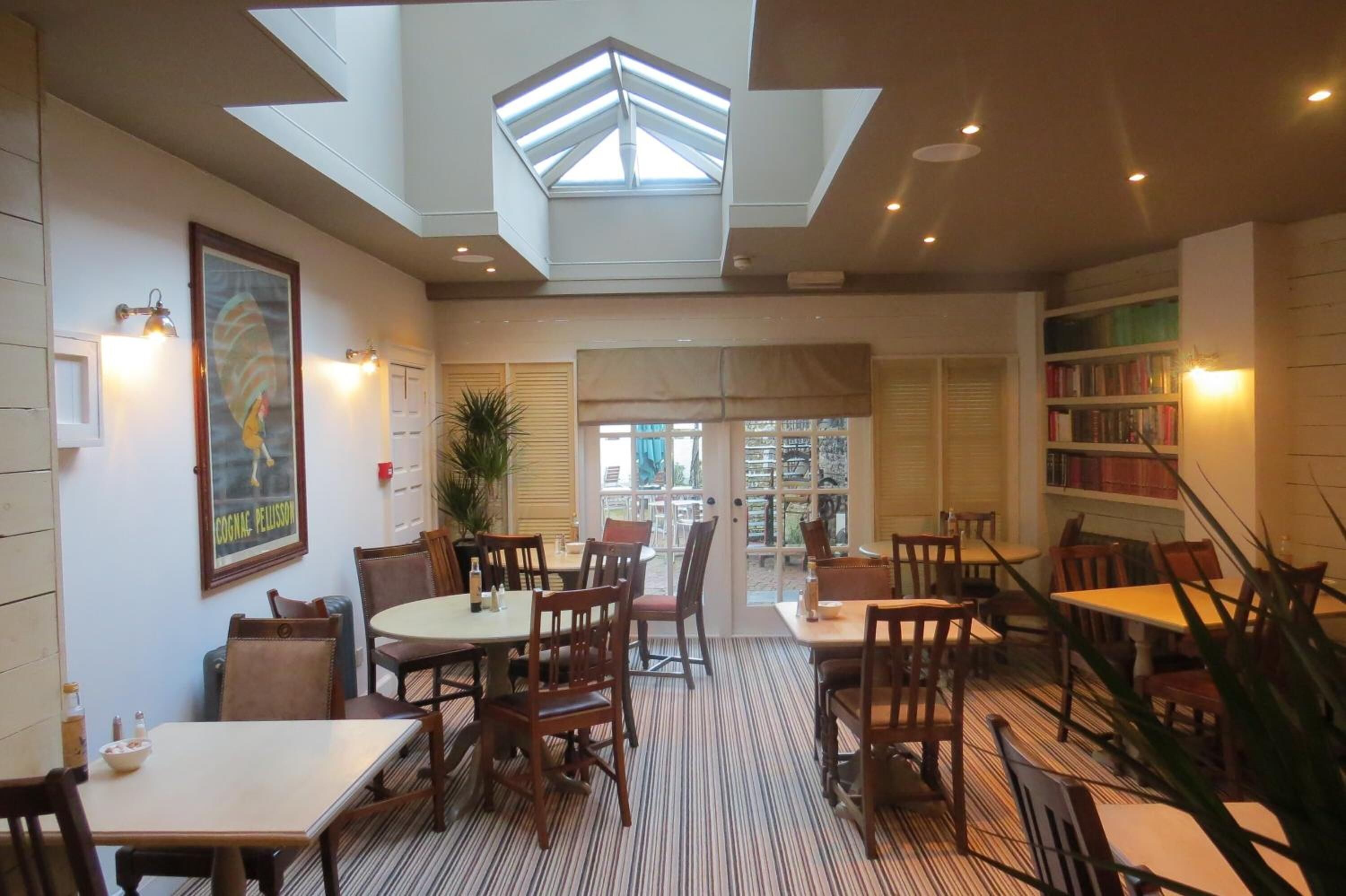 A spacious indoor area with tables and chairs, a skylight, and a bookshelf.