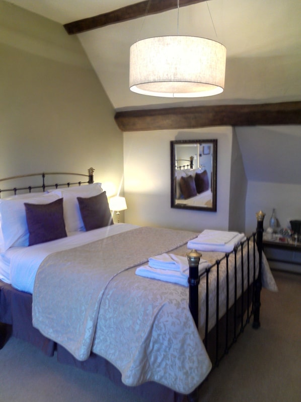 A neatly made bed with a headboard, a bedside lamp, and a mirror on the wall. - The Kings Head Hotel (Ross-on-Wye)