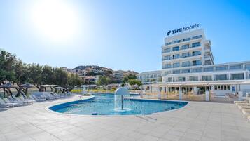 Zona de piscina de THB hotels con una fuente, tumbonas y vistas del edificio del hotel.