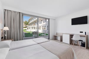 A hotel room with two beds, a desk, a chair, a TV, and a view of the outdoor area.