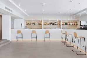Un moderno bar con una barra larga, varios taburetes y una variedad de botellas y copas.