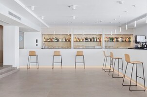 Un moderno bar con una barra larga, varios taburetes y una variedad de botellas y copas.