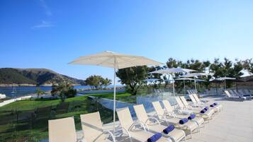 A poolside area with sun loungers and umbrellas, overlooking a body of water and hills.