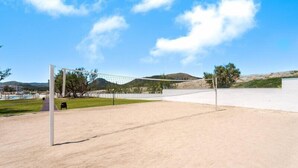 Una cancha de voleibol con red, rodeada por una zona de arena y un cielo despejado.