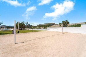 Un terrain de volley-ball avec un filet, entouré d’une zone sablonneuse et sous un ciel dégagé.