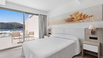 Habitación de hotel con una cama grande, un escritorio, una silla, vista al mar y un cuadro con conchas marinas.