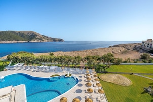 Una piscina con vistas al mar, rodeada de sillones y sombrillas.