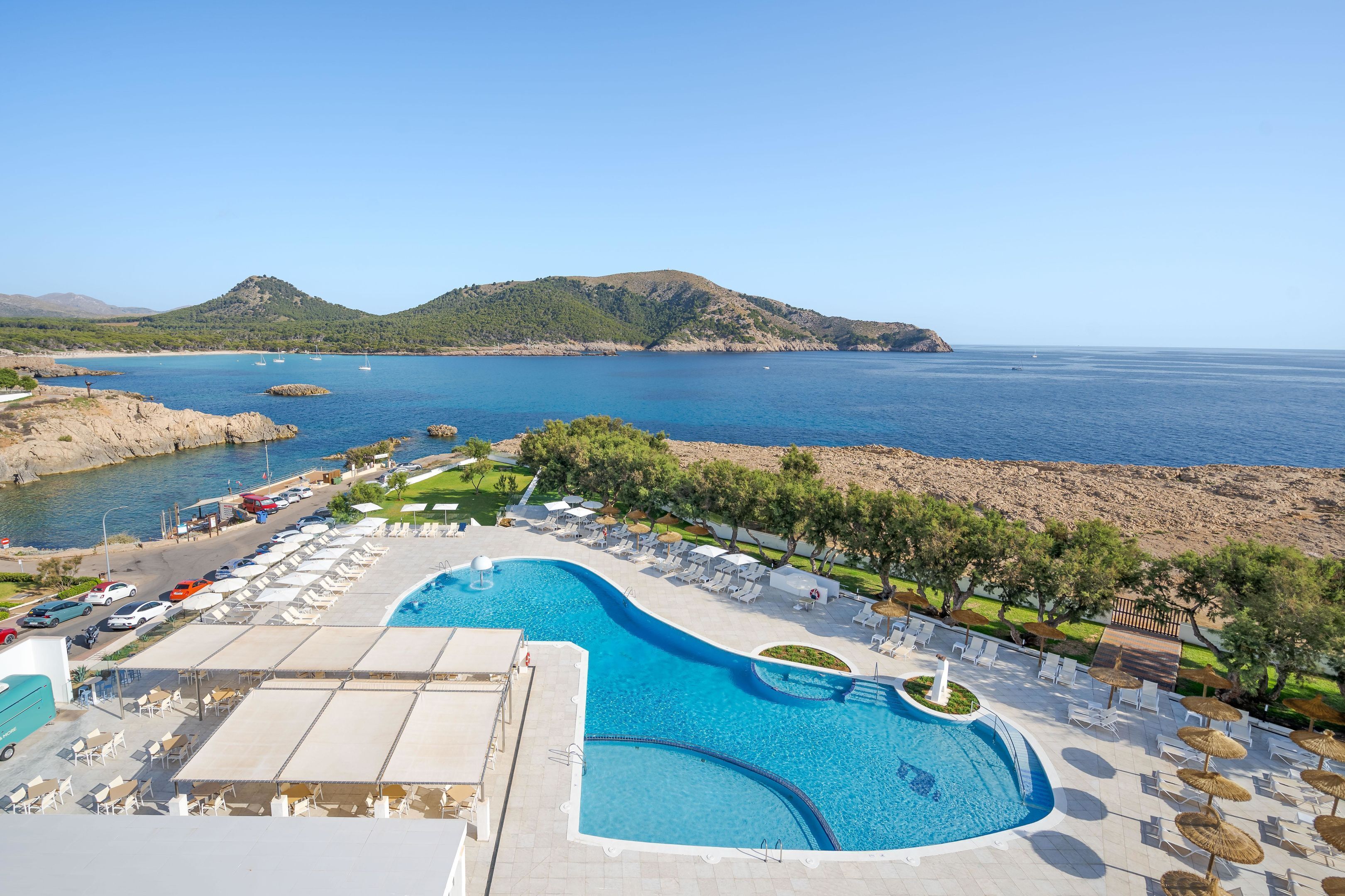 Un complexe hôtelier doté d’une grande piscine, de chaises longues et offrant une vue sur la mer et les collines.