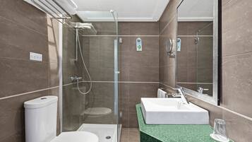 Ein modernes Badezimmer mit einer Glaskabine zur Dusche, einer weißen Toilette und einem Waschbecken mit grüner Arbeitsplatte.