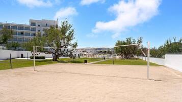 Un terrain de volleyball de plage, avec un filet, entouré d’arbres et avec un bâtiment visible au loin.