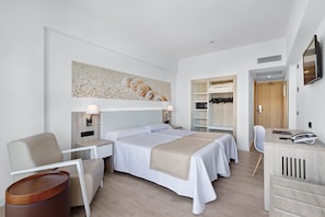 A modern hotel room with a large bed, a desk, a chair, and a wardrobe.