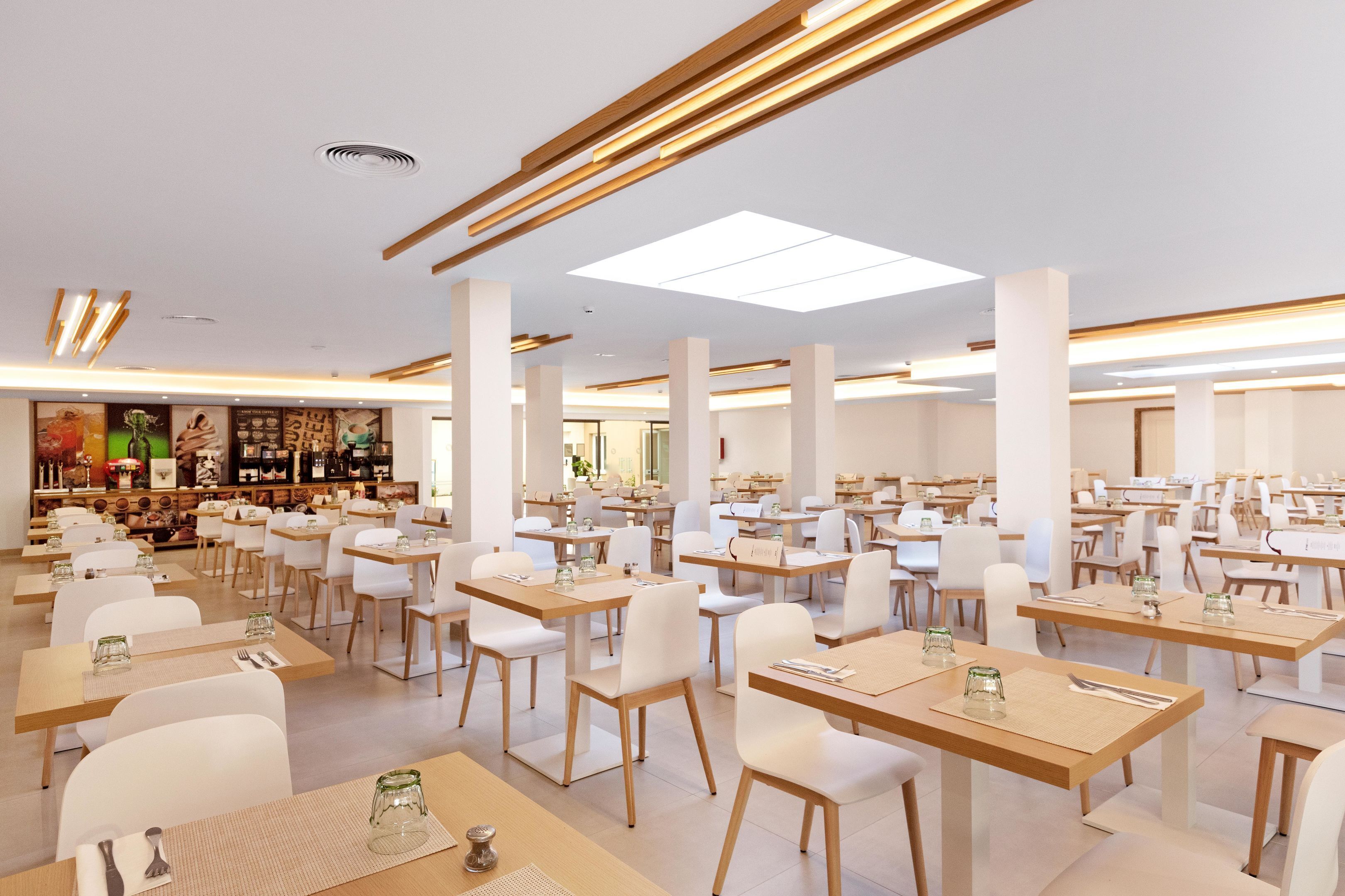 Un comedor espacioso con varias mesas y sillas, una zona de bar con distintos elementos y un diseño de techo moderno.