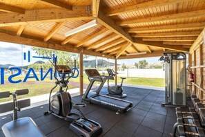 Une salle de sport couverte, équipée de matériel d’exercice, offrant une vue sur l’extérieur et sur laquelle on peut voir une pancarte dont le texte est partiellement visible.
