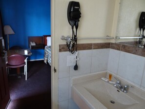 A hotel room with a bed, a desk, a chair, a sink, and a hairdryer on the wall.