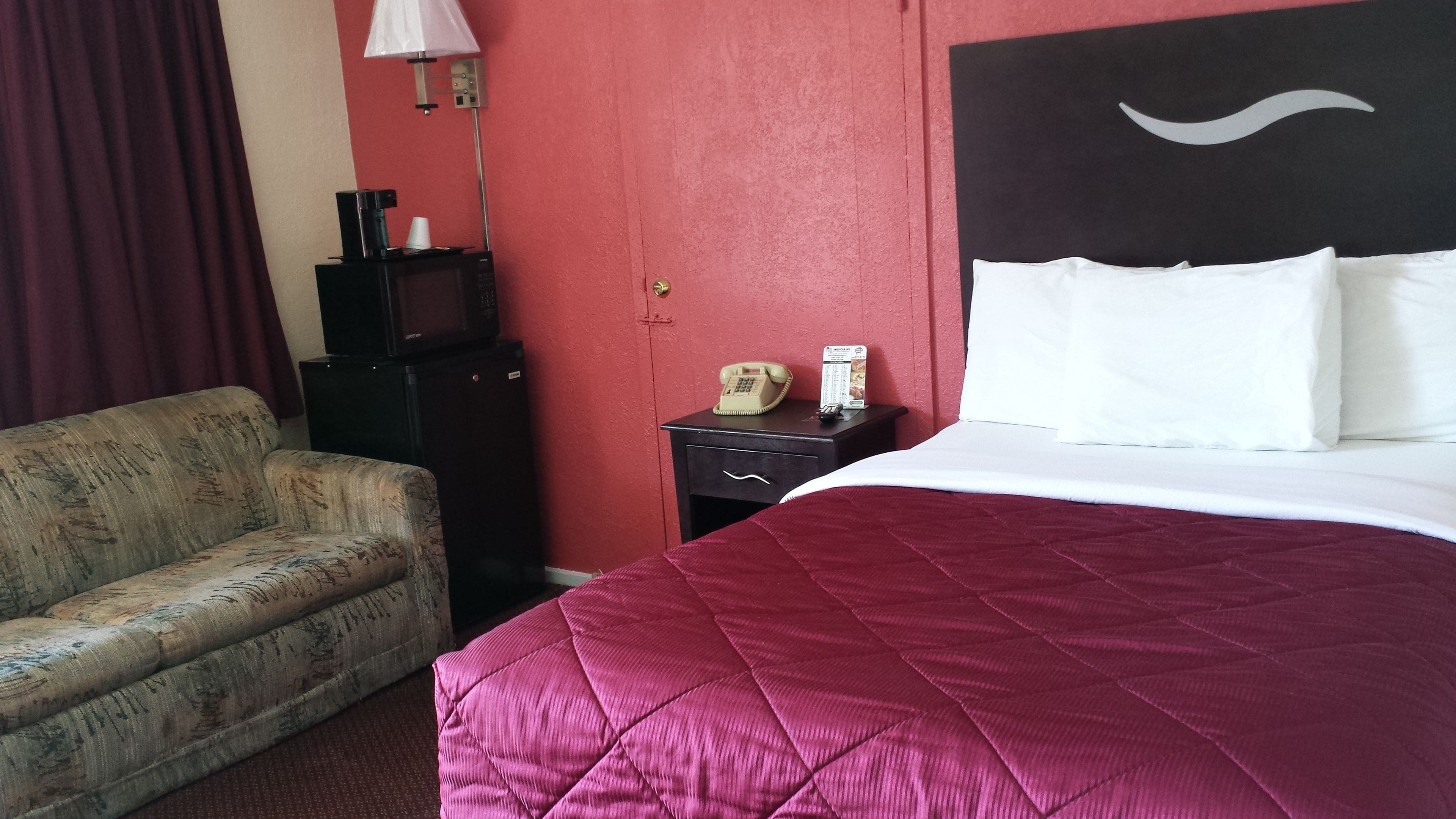 Habitació d'hotel amb llit, taulell de nit, telèfon, microones i sofà.