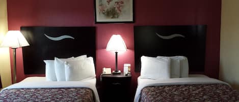 A hotel room with two beds, a nightstand with a lamp, a phone, and a framed picture on the wall.