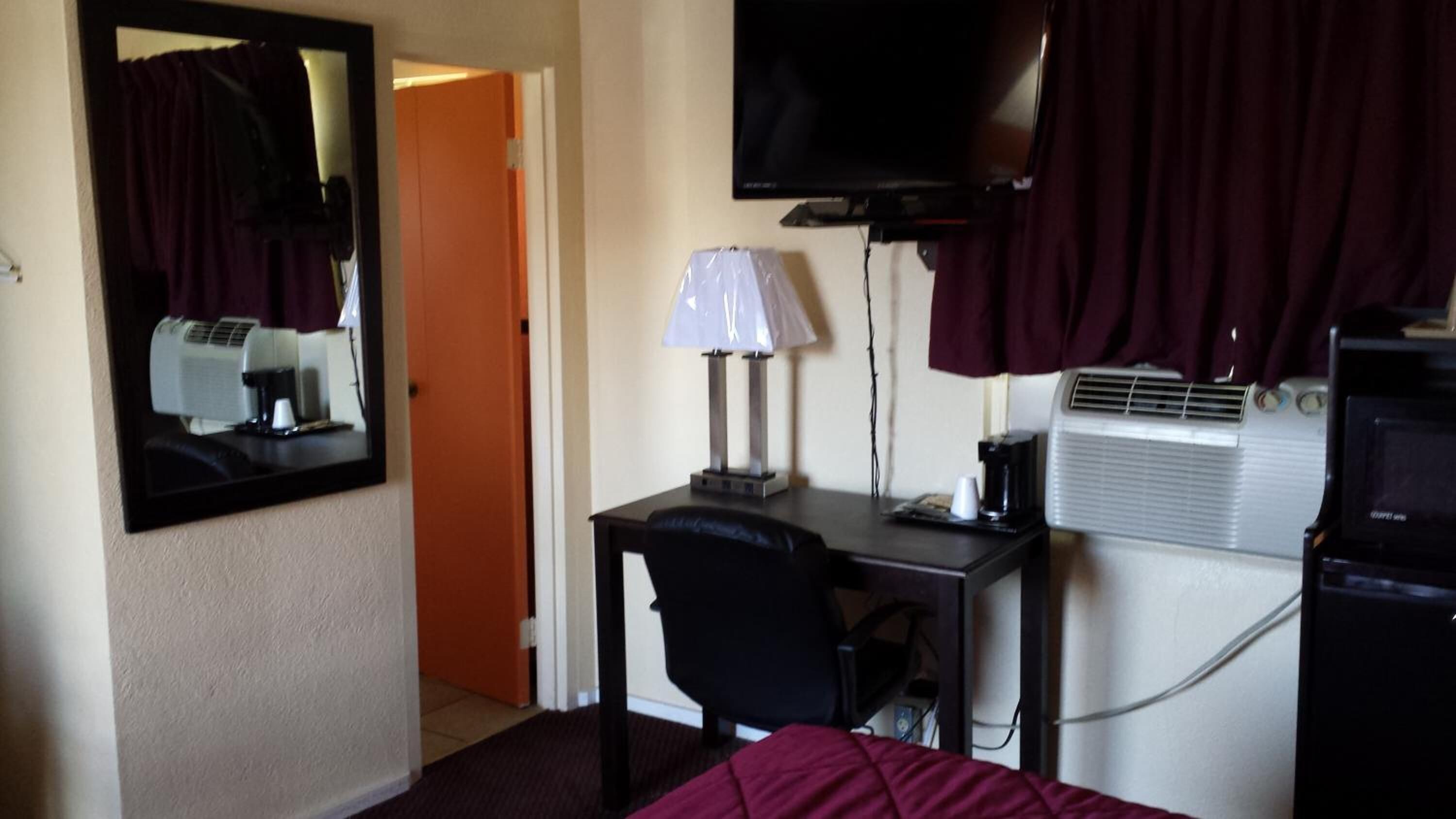 A hotel room with a desk, chair, TV, air conditioning unit, and a mirror.