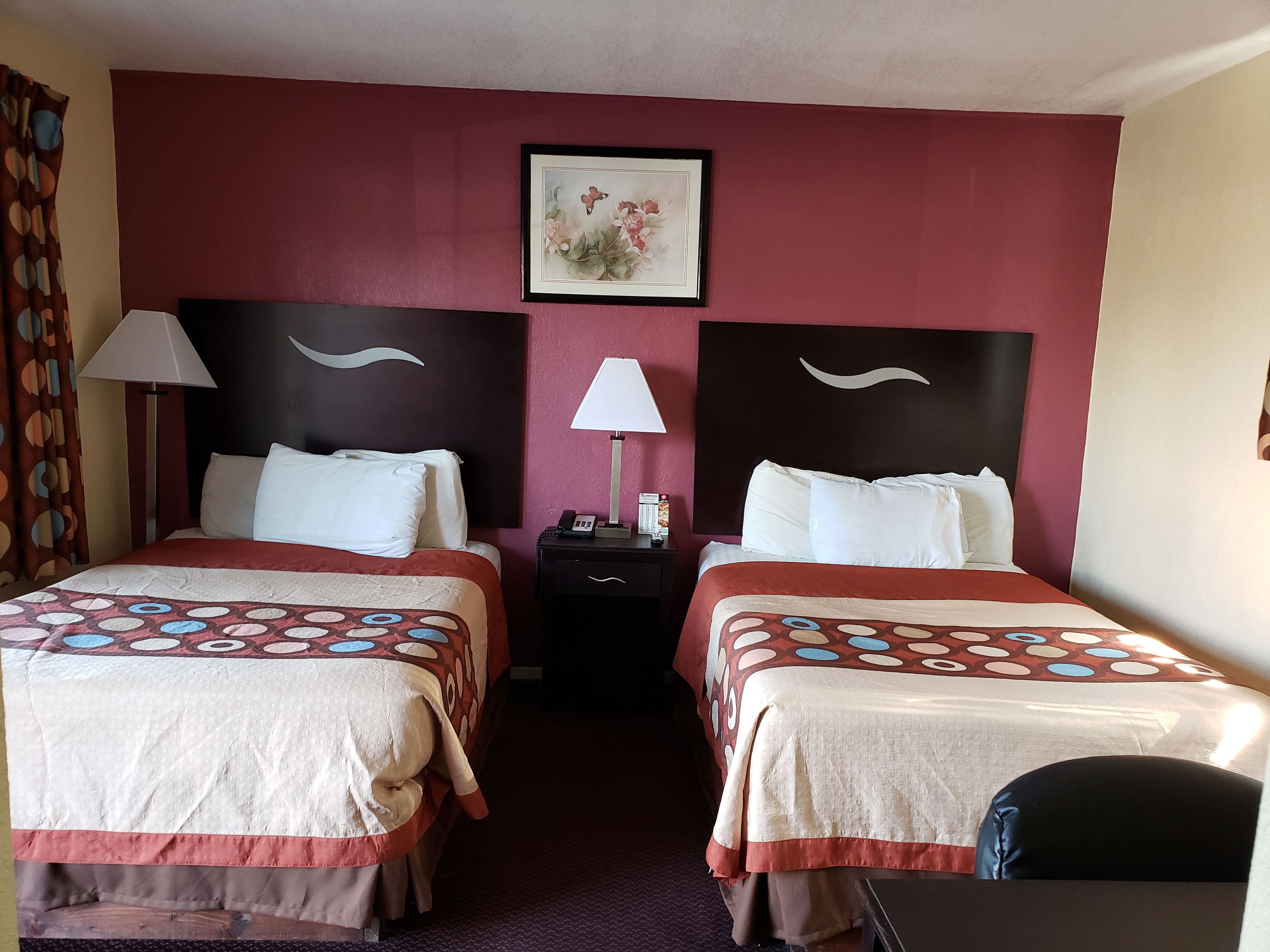 A hotel room with two beds, each with a patterned bedspread, a nightstand with a lamp, and a framed picture on the wall.