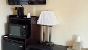 A hotel room with a desk, a black office chair, a television mounted on the wall, a microwave, a coffee maker, and a lamp. - American Inn Sedalia (Sedalia)