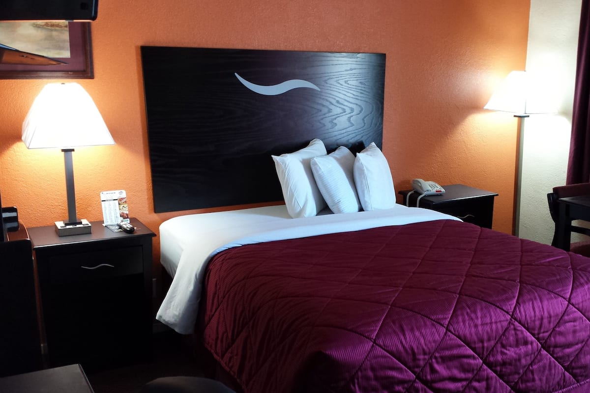 Una habitación de hotel con una cama, mesitas de noche, un escritorio y una lámpara.