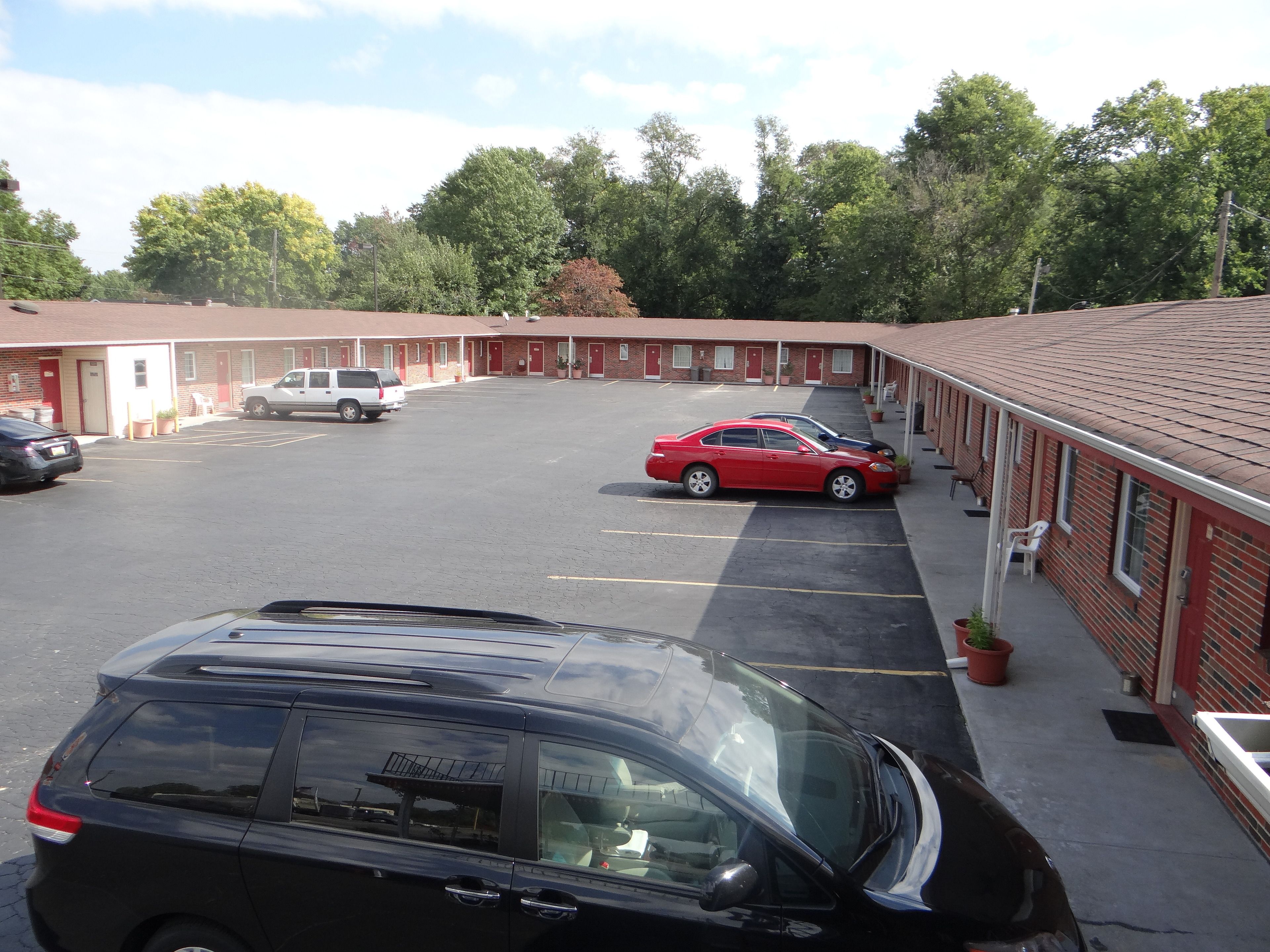 Un motel doté d’un parking, de plusieurs chambres et d’une voiture rouge garée sur le parking.